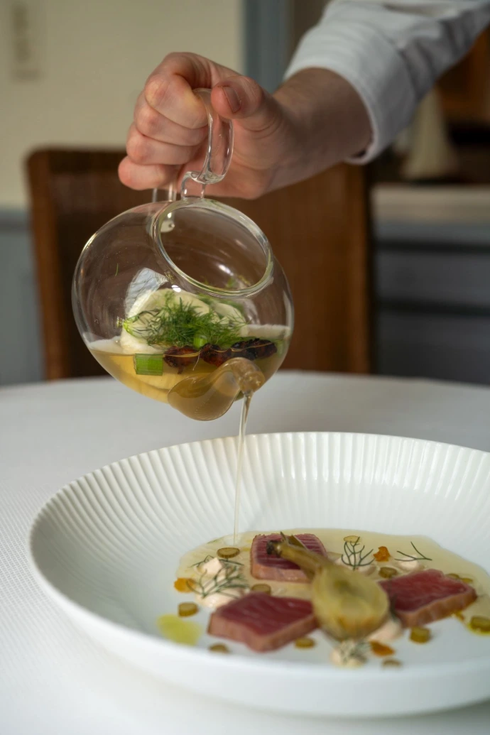 Le thon rouge, sélectionné pour sa qualité exceptionnelle, est ici sublimé dans une création tout en finesse. Associé à un bouillon délicatement infusé et versé à la minute, ce plat révèle toute la richesse des saveurs marines dans une mise en scène aussi spectaculaire que gourmande.  La fraîcheur du poisson, la précision des assaisonnements et la légèreté du consommé créent un équilibre parfait entre intensité et délicatesse. Chaque élément est pensé pour mettre en valeur le produit tout en offrant une expérience sensorielle unique.  Cette assiette incarne l’esprit de notre cuisine gastronomique : des produits d’exception, une technique maîtrisée et une recherche constante d’émotion à travers le goût.